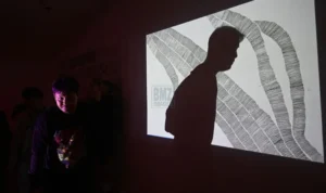 Pengunjung berjalan di depan salah karya visual yang dipantulkan ke dinding pada pameran Mutuals "Garis Mencurigakan" di Galeri Marlah Hub di Palu, Jumat (1011/7/2025). (bmzIMAGES/basri marzuki)